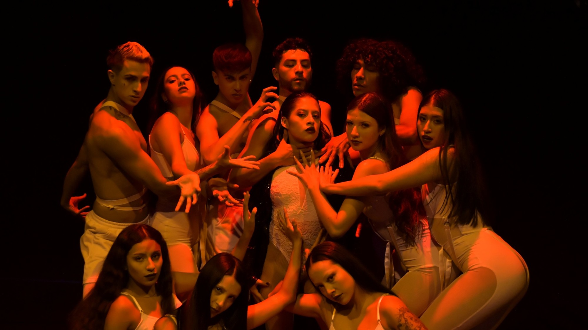 Latino Talent Agency dance ensemble in white costumes posing together under red stage light